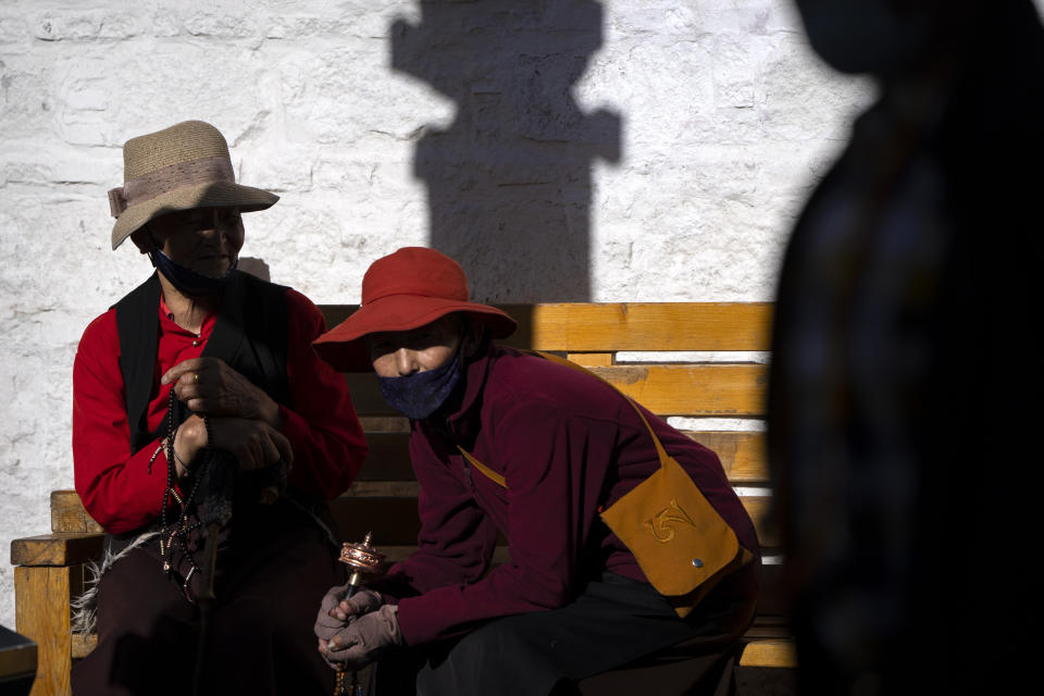 Members of the Buddhist faithful hold beads and a prayer wheel as they sit on a bench outside the Jokhang Temple in Lhasa in western China's Tibet Autonomous Region, Tuesday, June 1, 2021, as seen during a government organized visit for foreign journalists. High-pressure tactics employed by China's ruling Communist Party appear to be finding success in separating Tibetans from their traditional Buddhist culture and the influence of the Dalai Lama. (AP Photo/Mark Schiefelbein)