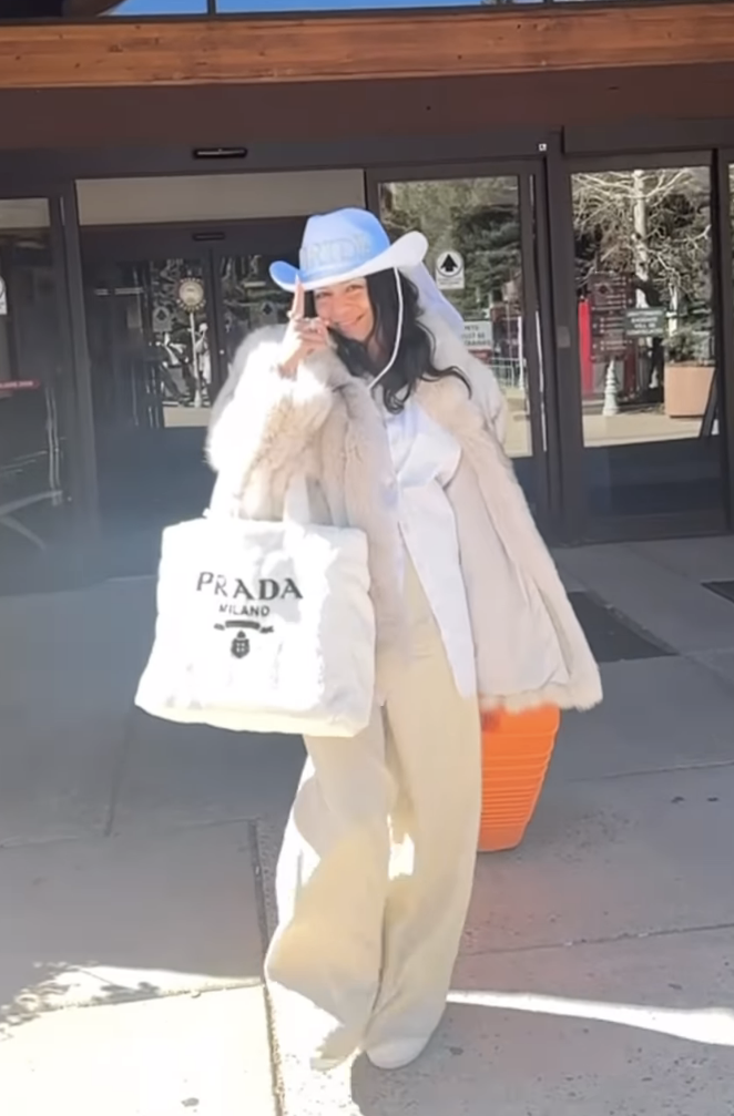 Close-up of Vanessa on the street wearing a Western-style hat and carrying a Prada shopping bag