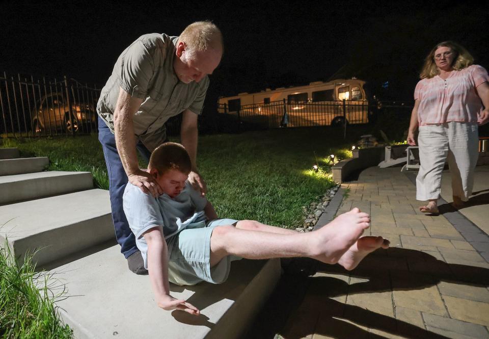 Glenn Maughan catches and supports his son Glenn Maughan, nicknamed Bug, as Bug has a tonic seizure outside of their home in Manchester, Md., on Saturday, July 8, 2023. Annette Maughan rushes in to help. Bug, age 20, has KBG syndrome. He is nonverbal and currently experiences one to three seizures a day. Bug was sitting down as his seizure started, and his father was standing behind him just in case it happened, so that he wouldn’t fall back and hit his head on the steps. | Kristin Murphy, Deseret News