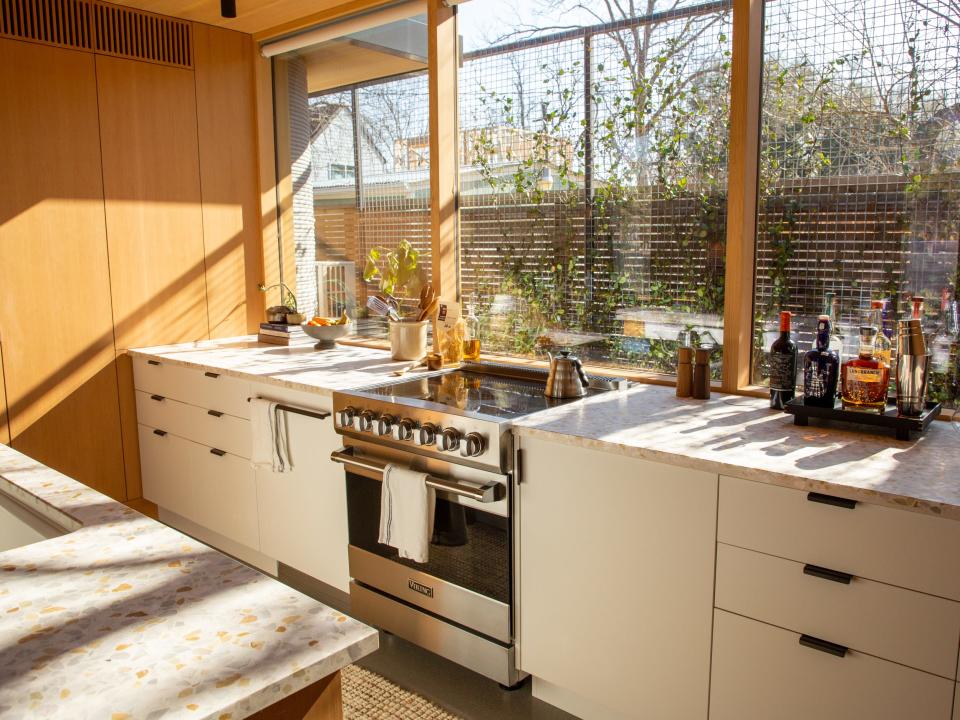 A kitchen filled with natural light from the windows. There are features like drawers, a stove and oven, and bar items.