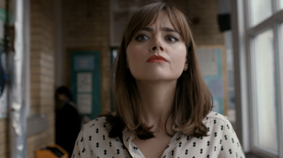 Jenna Coleman stands indoors, looking upward, wearing a patterned blouse