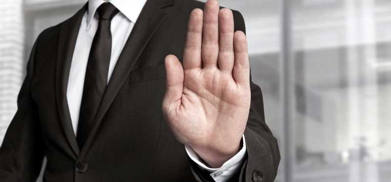 Man in business suit holds up his hand as if to indicate stop.