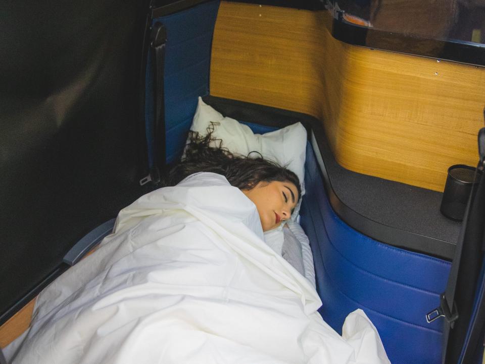 A person sleeping on a bed surrounded by short blue and yellow walls on a Napaway bus.