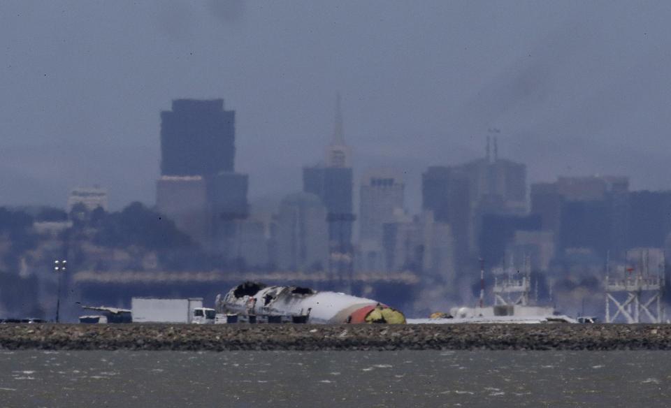 The wreckage of Asiana Flight 214, which crashed on Saturday, July 6, 2013, is seen on a tarmac in front of the San Francisco skyline at San Francisco International Airport in San Francisco, Wednesday, July 10, 2013. Investigators are struggling to piece together what went wrong in an accident that left two of the 307 aboard dead and close to 20 seriously injured. (AP Photo/Jeff Chiu)