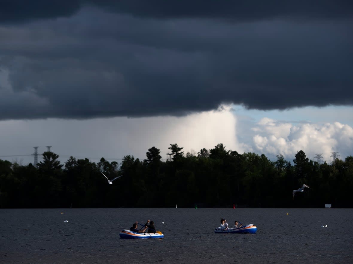 Storm clouds are seen in the distance as people paddle inflatable boats at Mooney's Bay in Ottawa in May 2020. It's best to get to land as quickly as possible when a storm approaches. (Justin Tang/Canadian Press - image credit)