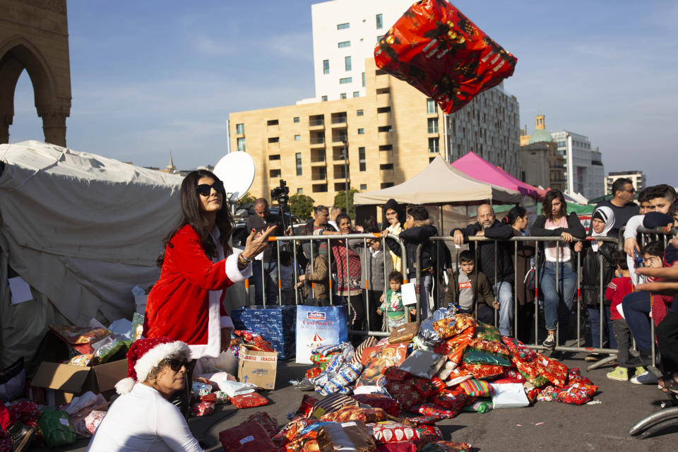 In this Sunday, Dec. 22, 2019, photo, volunteer Ibtisam Nablussi tosses a Christmas present, as anti-government protesters distribute clothing to the needy ahead of Christmas, at Martyrs Square in Beirut, Lebanon. Lebanon is entering its third month of protests, the economic pinch is hurting everyone, and the government is paralyzed. So people are resorting to what they've done in previous crises: They rely on each other, not the state. (AP Photo/Maya Alleruzzo)