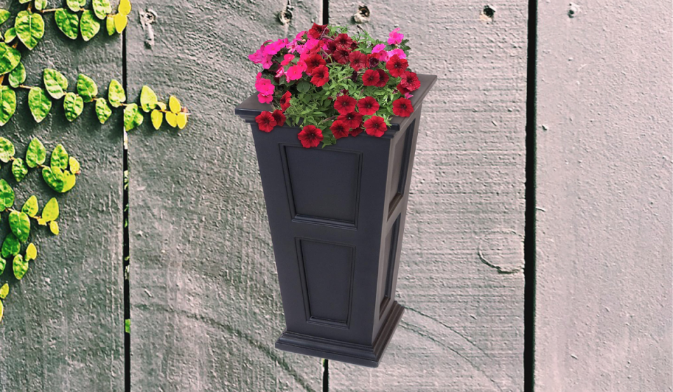 A tall black planter with red and pink flowers inside