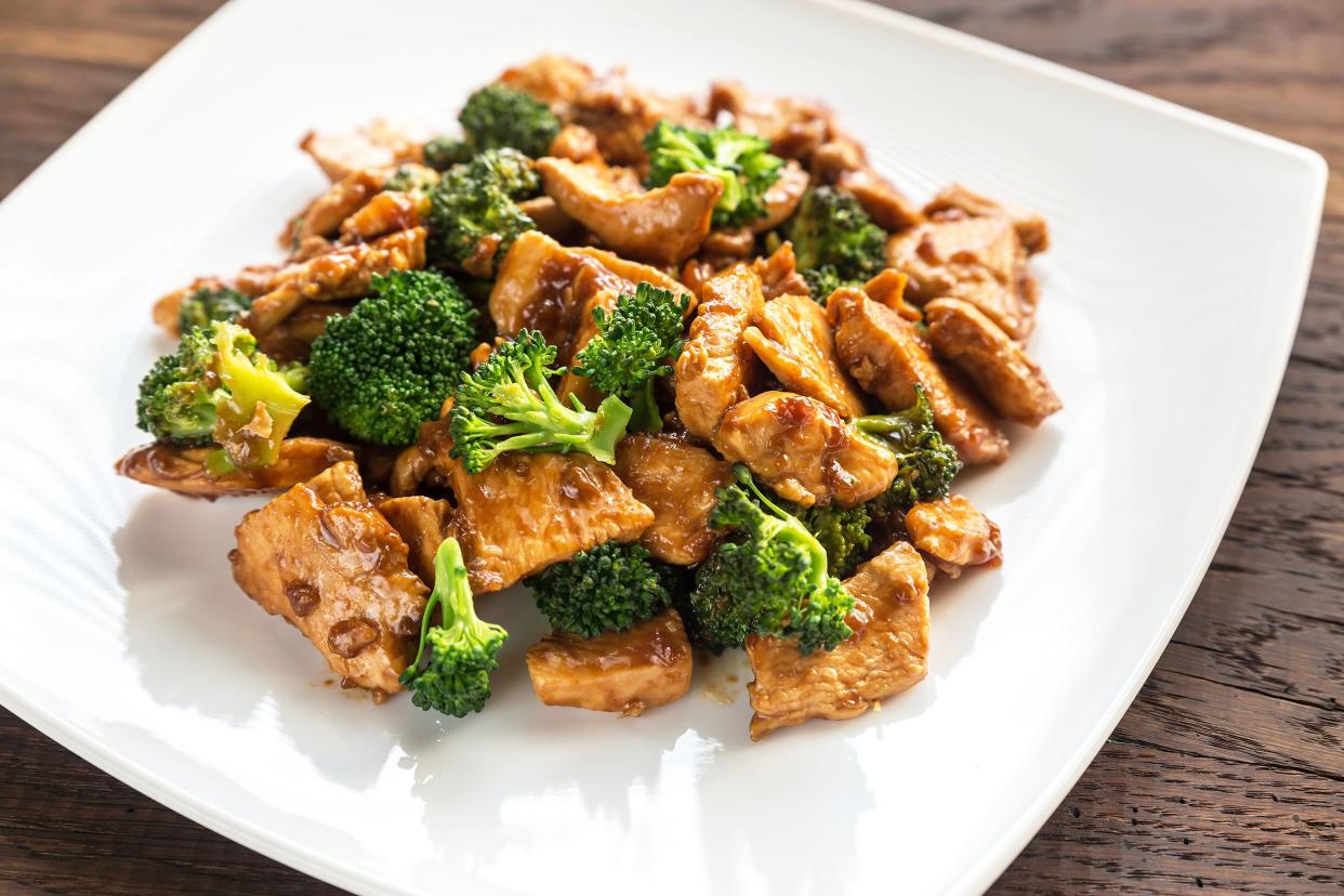 Chicken and broccoli stir fry on a white plate on a wooden table