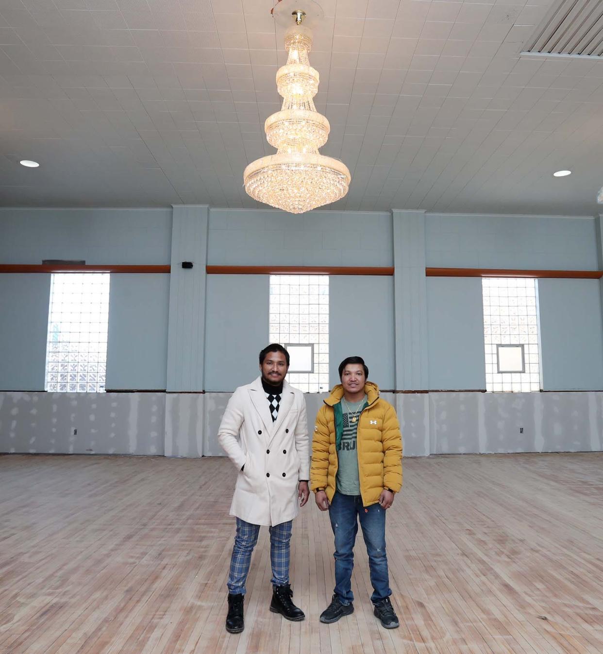 Som Baraily, left, and Janga Gajmer, owners of the Namaste Center formerly the Italian Center on East Tallmadge Avenue, stand under the new chandelier in the banquet hall they are renovating on Monday in Akron. 