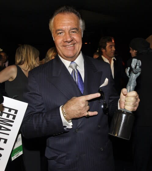 A man in a suit holds an acting trophy
