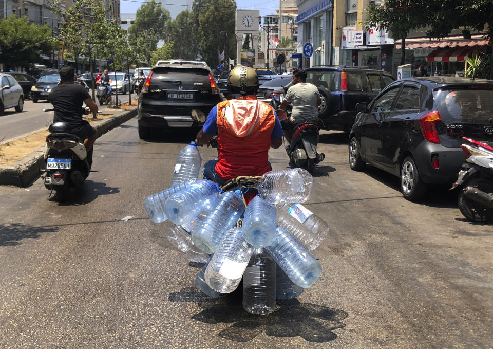 A man rides his scooter with empty water bottles to fill them with gasoline, in Beirut, Lebanon, Wednesday, June 23, 2021. Lebanon is struggling amid a 20-month-old economic and financial crisis that has led to shortages of fuel and basic goods like baby formula, medicine and spare parts. The crisis is rooted in decades of corruption and mismanagement by a post-civil war political class. (AP Photo/Hussein Malla)