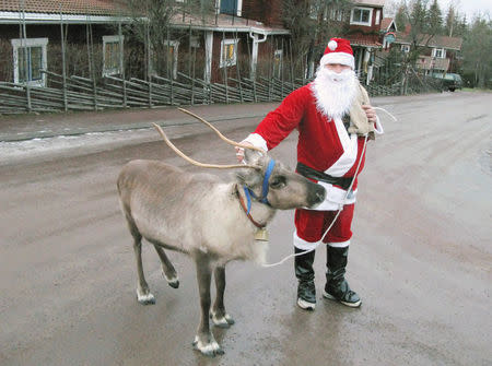 A man dressed as Santa Claus walks his pet reindeer as he visit hotels and shops in Tallberg, Sweden, December 24, 2006. REUTERS/Shaun Best/File Photo