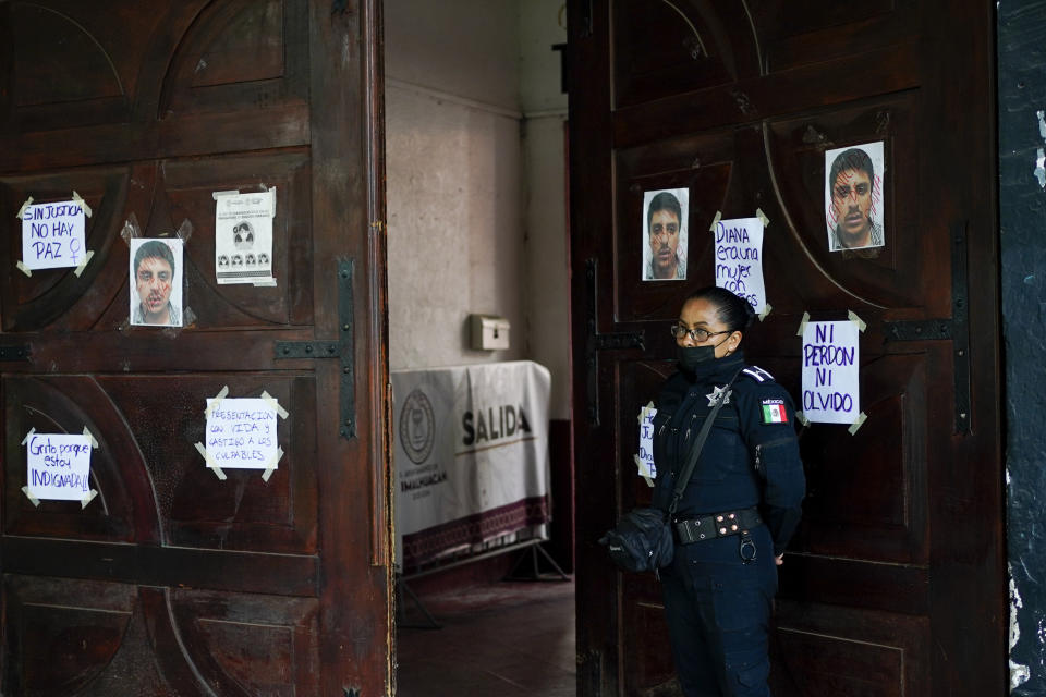 A policewoman guards the Mayor's office door covered with photographs of Jesús Alejandro Montes Moreno, the convicted murderer of Diana Velazquez in Chimalhuacan, State of Mexico, Mexico, Saturday, July 2, 2022. The 24-year-old candy vendor was making a call outside her home in 2017 when she went missing. She was later found beaten, raped and strangled. Mont was sentenced to 93 years in prison for femicide. (AP Photo/Eduardo Verdugo)