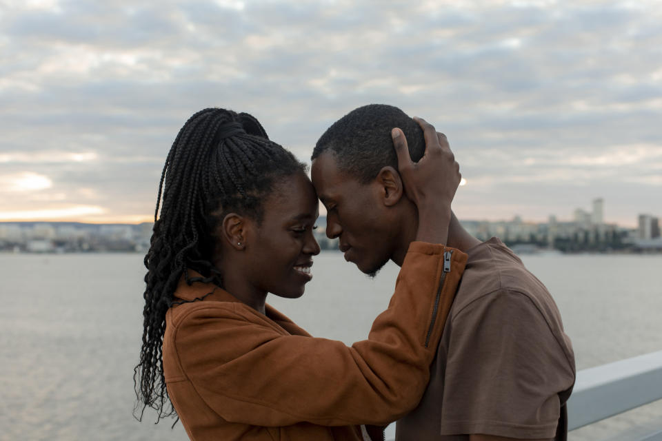 Two people affectionately touching foreheads by a lakeside at dusk, sharing a moment of connection