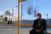 A man wearing a protective face mask, following the outbreak of coronavirus disease (COVID-19), sits at a bus stop in Qom