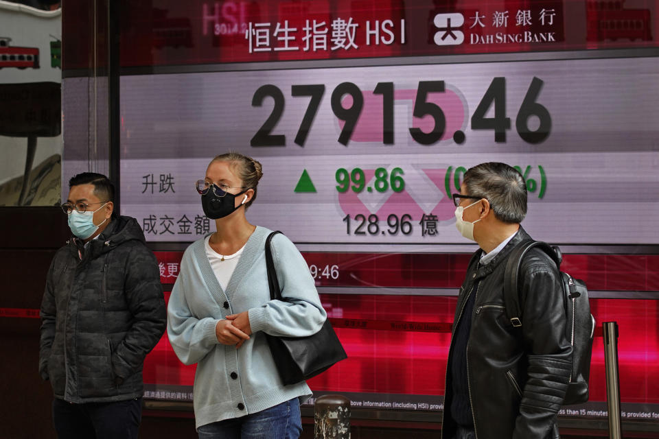 People walk past a bank electronic board showing the Hong Kong share index at Hong Kong Stock Exchange Monday, Feb. 17, 2020. Markets are mixed in Asia, with Japan's benchmark slipping 0.8% after the government reported the economy contracted in the last quarter. (AP Photo/Vincent Yu)