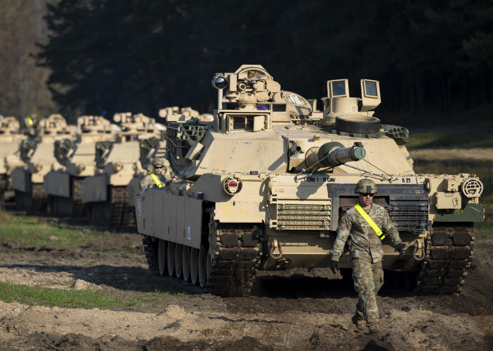 A U.S. Army soldier walks near a line of Abrams battle tanks.