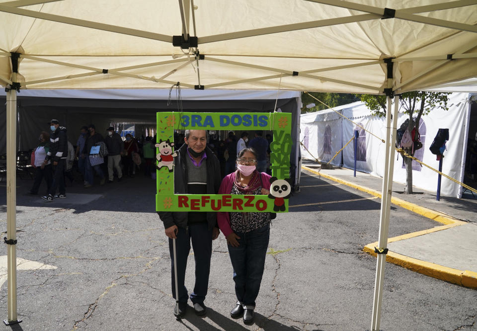 A couple poses for a photo holding a frame with a message that reads in Spanish: "Third dose, get vaccinated, reinforcement", after receiving an AstraZeneca booster against COVID-19 during a vaccination campaign for people 60 and over, in Mexico City, Tuesday, Jan. 4, 2022. (AP Photo/Fernando Llano)