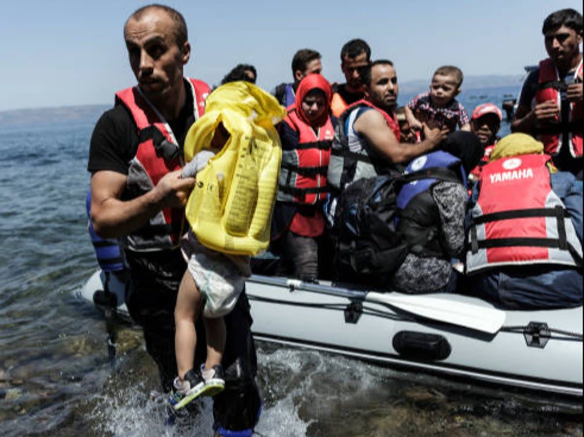 A Syrian migrant helps children get off an inflatable boat after it arrived on the Greek island of Lesbos after crossing the Aegean sea from Turkey to Greece  (AFP via Getty Images)