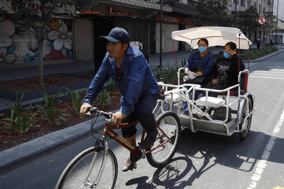 Mujeres con máscaras protectoras viajan en un taxi bicicleta en el centro de la Ciudad de México, el lunes 6 de abril de 2020. (AP Foto/Rebecca Blackwell)