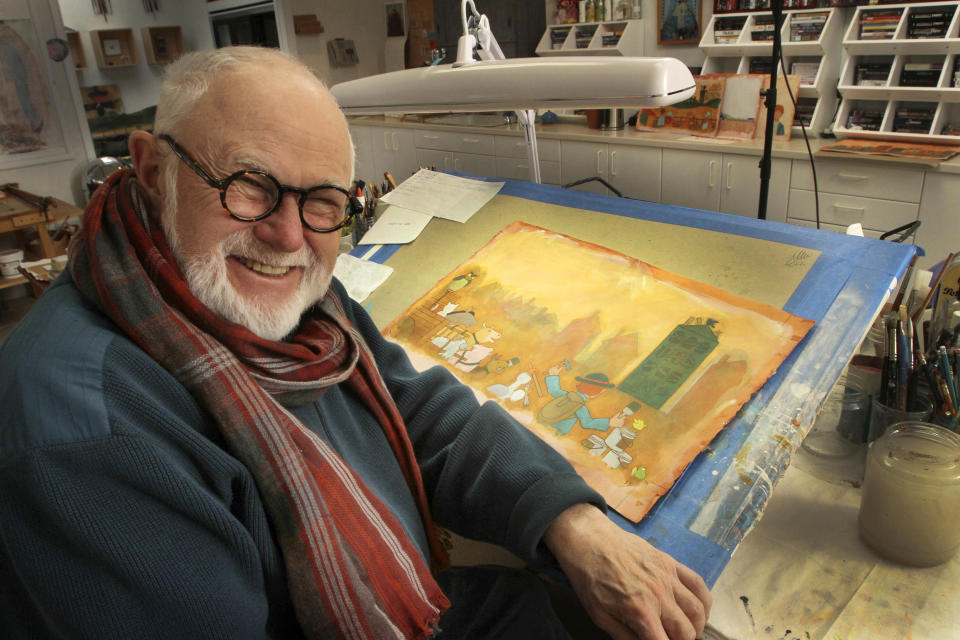 In this photo taken Sunday Dec. 1, 2013, Tomie dePaola poses with his artwork in his studio in New London, N.H. The beloved children's author and illustrator has died at the age of 85. DePaola delighted generations with tales of Strega Nona, the kindly and helpful old witch in Italy. His literary agent says dePaola died Monday from surgery complications after taking a bad fall last week. (AP Photo/Jim Cole, File)