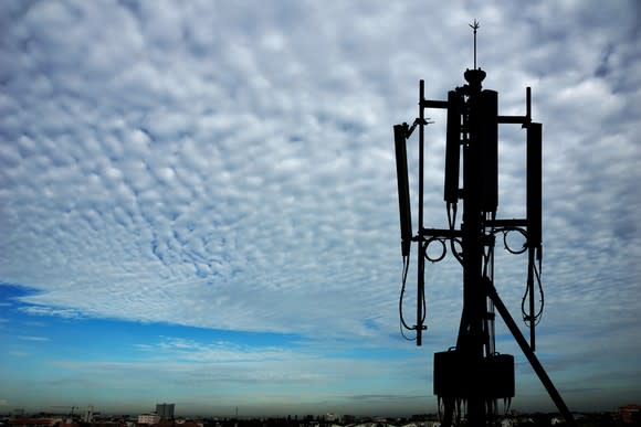 Silhouette of a piece of transmission equipment on a cell tower, set against blue skies and fluffy clouds