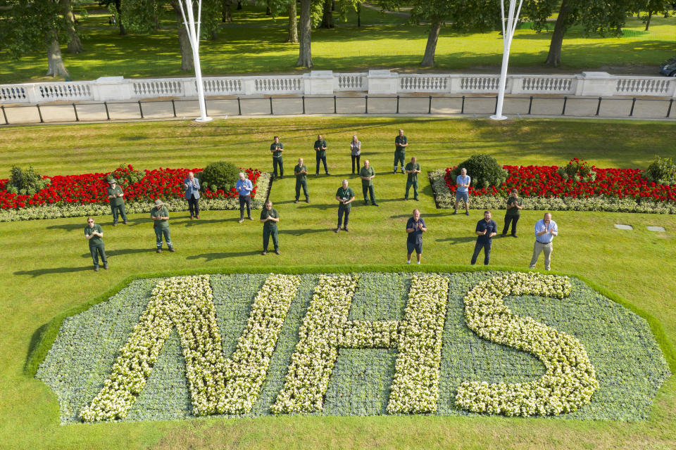 Royal Parks staff applaud the NHS's 72 birthday behind one of two specially created 12 x 5 metre flowerbeds in front of Buckingham Palace in the Memorial Gardens in St James's Park. The letters are made up of 1,500 Begonia semperflorens 'Heaven White' plants in each bed, while the background is 21,000 plants of Echeveria imbricate, Senecio serpens and Sedum pachyclados.