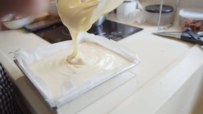 pouring white cake batter into cake tin