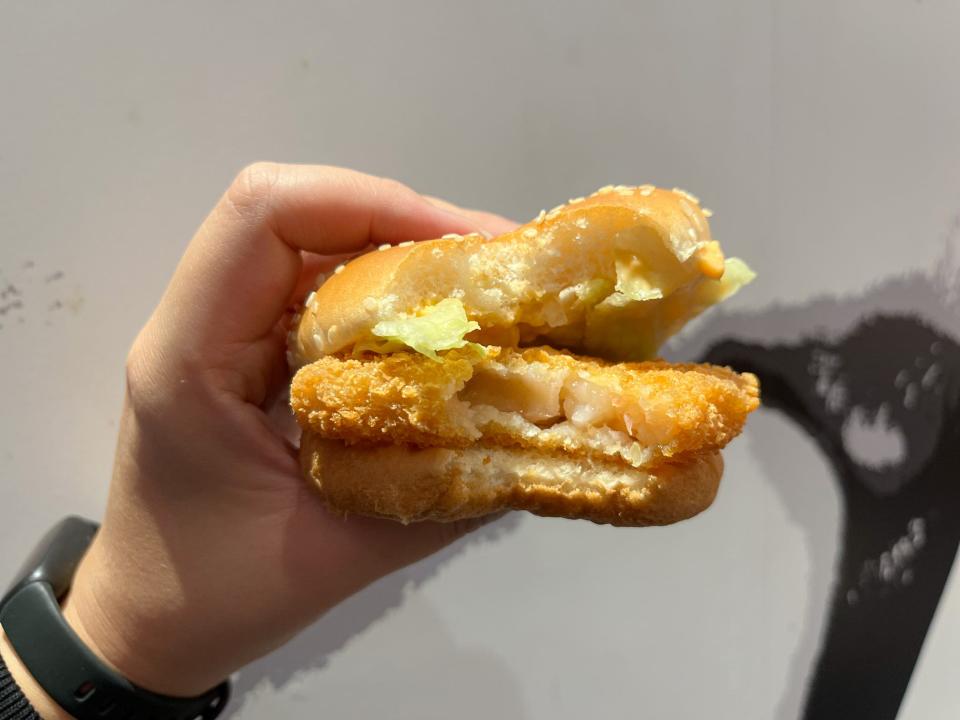 A hand holding a breaded patty on a bun with a bite taken out of it.