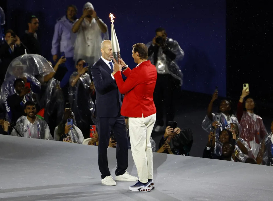 2024巴黎奧運開幕式聖火傳遞， 法國前足球員席丹 (Zinedine Zidane)傳遞給西班牙網球選手納達爾 (Rafael Nadal) （照片來源：REUTERS/Anushree Fadnavis）