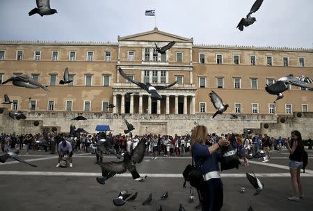 Tourists stand in front of the parliament building as pigeons fly by in Athens April 27, 2015. REUTERS/Alkis Konstantinidis