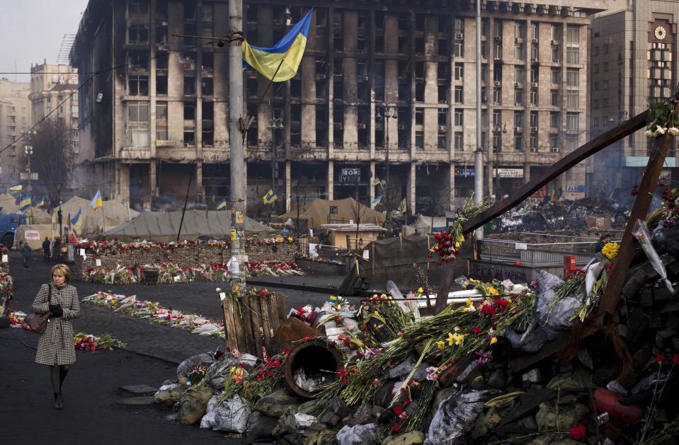 A woman walks past a barricade covered in flowers left to those killed in recent clashes in Kiev's Independence Square, Ukraine, Friday, March 7, 2014. In the background is the Trade Unions Building, which was damaged in a fire in late February. (AP Photo/David Azia)