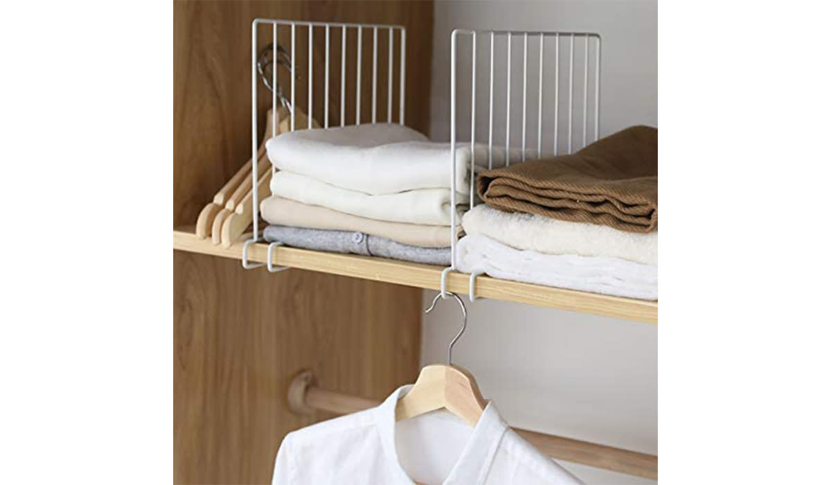 Two white shelf dividers between stacks of clothes on a closet shelf