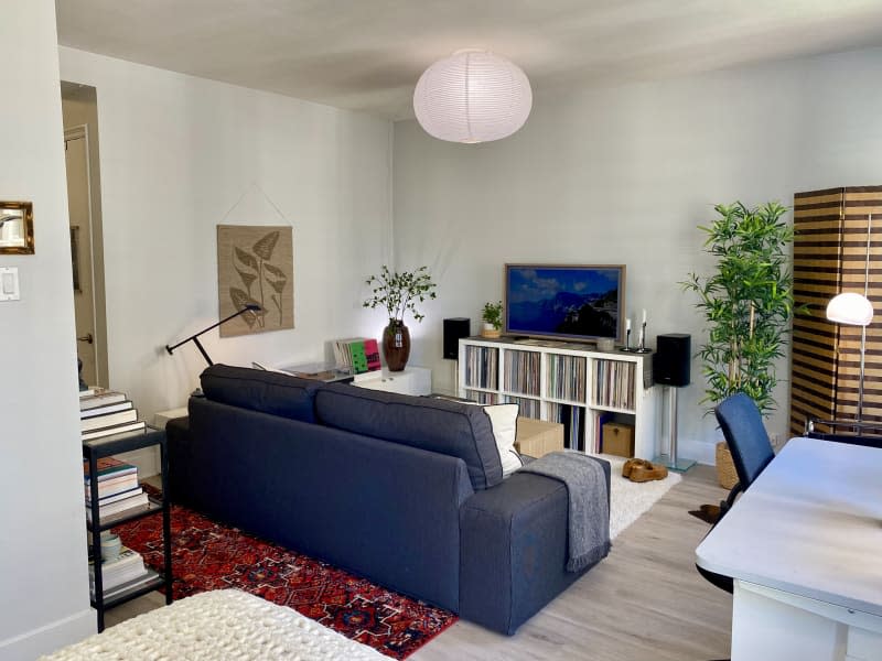 A grey couch in a white living room with a red area rug and record collection.