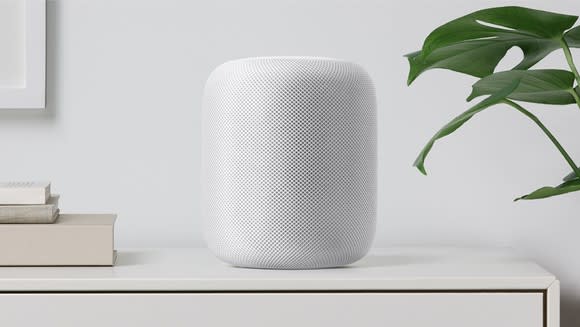 Apple HomePod sitting on a shelf next to books.