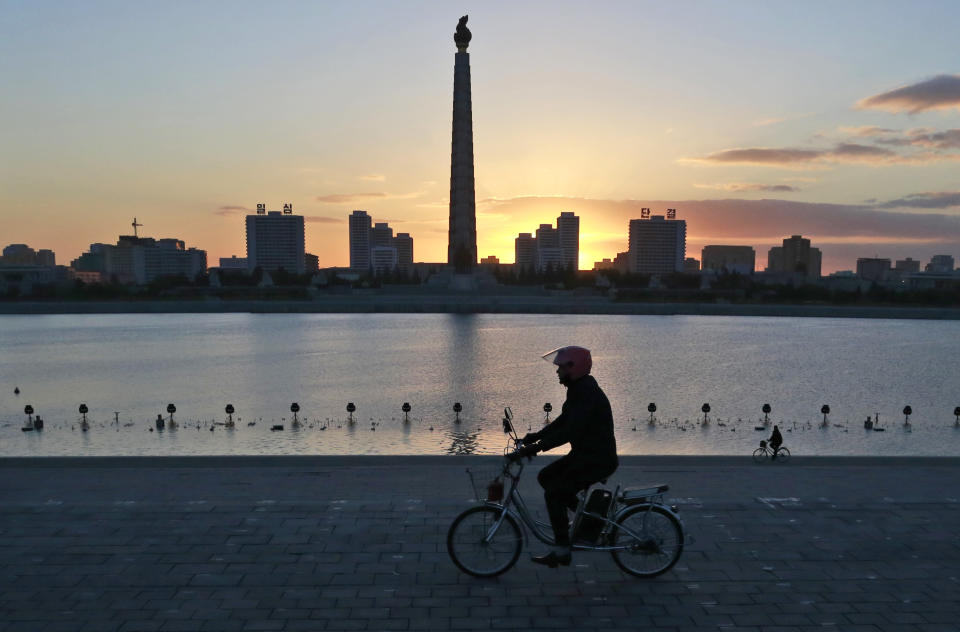 FILE - In this Oct. 27, 2018 file photo, a man rides his electric bike as the Tower of the Juche Idea is silhouetted agains the sunrise in Pyongyang, North Korea. As Chinese President Xi Jinping makes an official trip June 20, 2019 to North Korea, Beijing is anxious to encourage North Korea's self declared shift away from nuclear confrontation toward economic development. (AP Photo/Dita Alangkara, File)