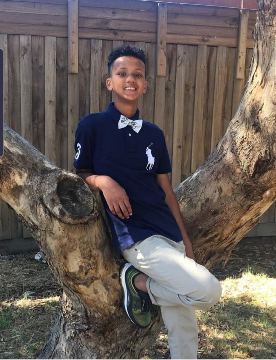 Kofi Aden is pictured wearing a bowtie while leaning against a tree.