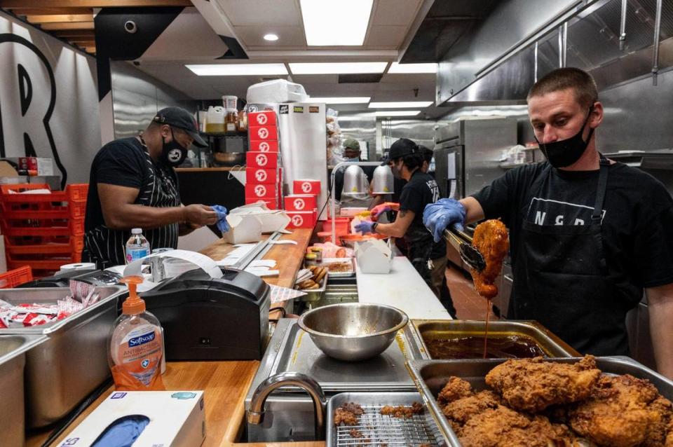 Owner Cecil Rhodes, left, works on orders while Matt Rocha, right, lifts a chicken thigh out of hot oil and Gavin Okamoto, center, makes sandwiches at Nash and Proper’s new takeout restaurant on K Street in downtown Sacramento on Thursday, Sept. 24, 2020.