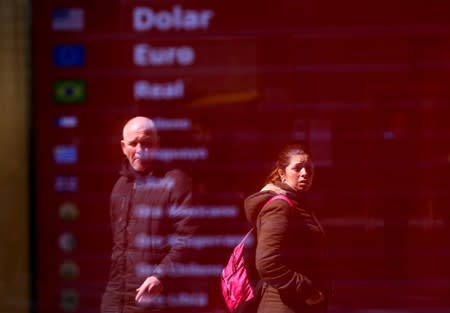 People are reflected in an electronic board that shows currency exchange, in Buenos Aires