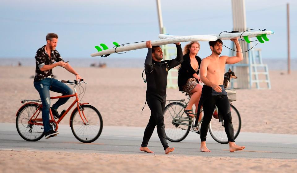 Surfers carry their boards as cyclists ride past, none wearing a face mask, at Santa Monica Beach near Santa Monica Pier, which re-opened with safety guidelines June 25.