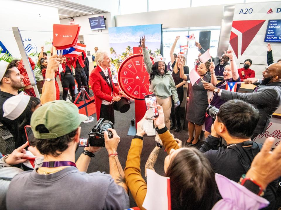 A crowded gate full of cheering people with Richard Branson in the middle next to a red wheel