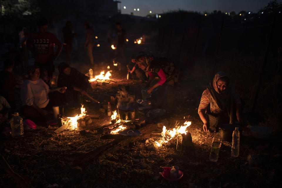 Refugees and migrants cook on makeshift fires near an abandoned factory in the island of Lesbos, Greece, Friday, Sept. 11, 2020. Thousands of refugees and migrants have spent a third night in the open on the Greek island of Lesbos after two consecutive nights of fires in the notoriously overcrowded Moria camp left them homeless. (AP Photo/Petros Giannakouris)