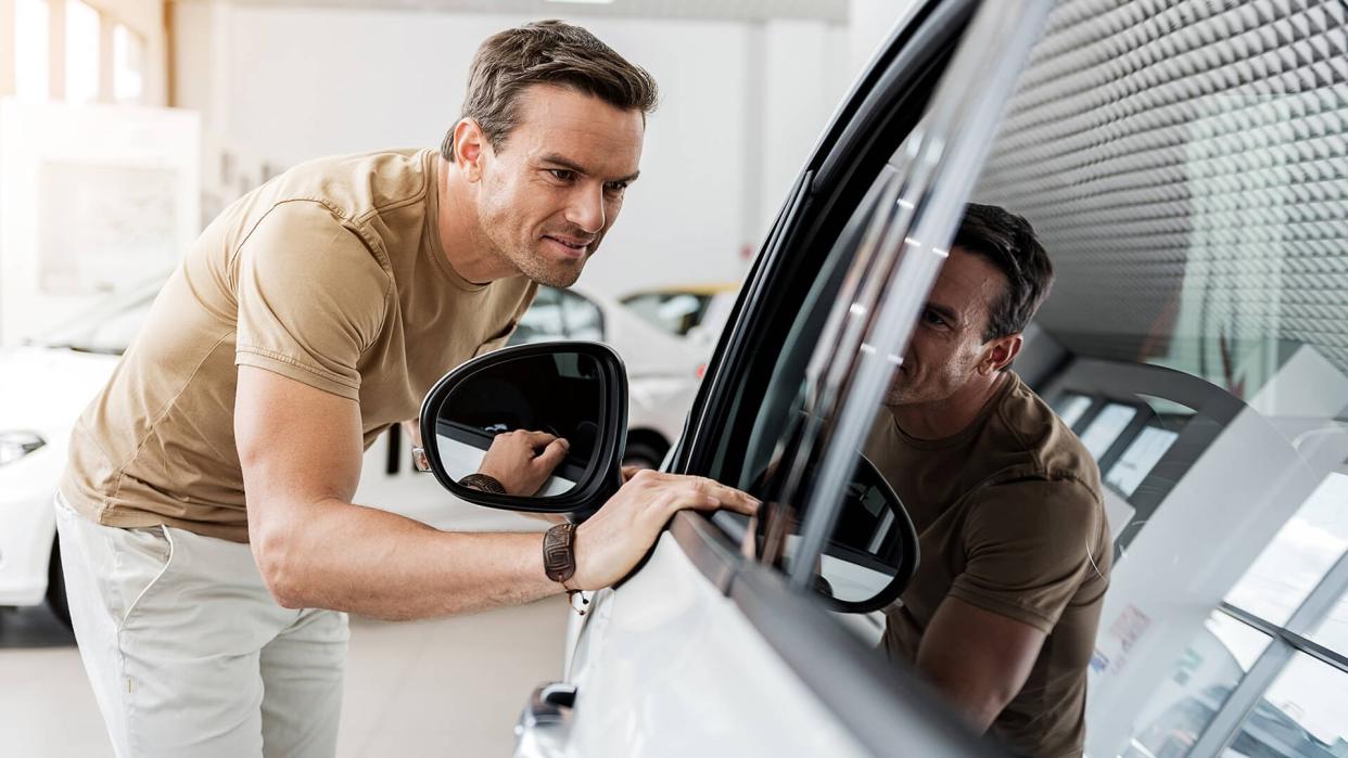 Smiling man expressing concernment while looking at passenger compartment through window of automobile.