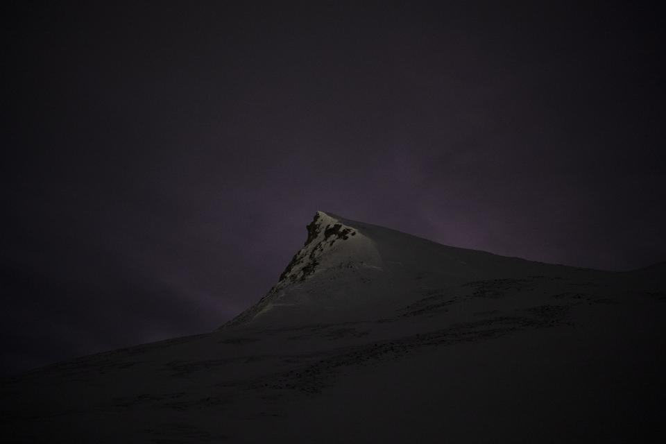 Luces en el cielo de la noche polar iluminan la cumbre de la montaña Plataberget en Longyearbyen, Noruega, el miércoles 11 de enero de 2023. Tan cerca del Polo Norte, el sol está al menos seis grados bajo el horizonte de mediados de noviembre hasta finales de enero. (AP Foto/Daniel Cole)