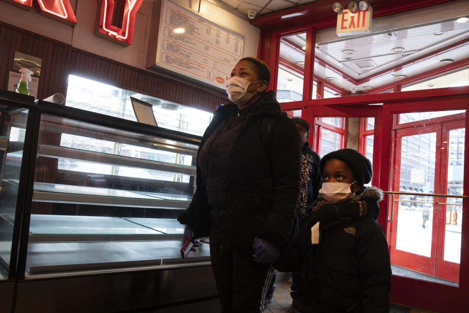 An employee of Junior's Restaurant arrives with her son to pick up a paycheck, Thursday, March 19, 2020 in the Brooklyn borough of New York. The restaurant company, which has closed its four locations due to the coronavirus, has laid off 650 of 850 employees. (AP Photo/Mark Lennihan)