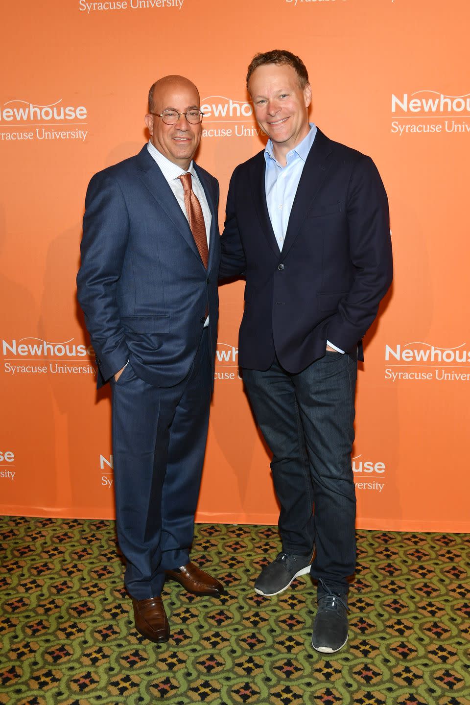 jeff zucker and chris licht, both wearing suits, smile for the camera while standing in front of an orange wall