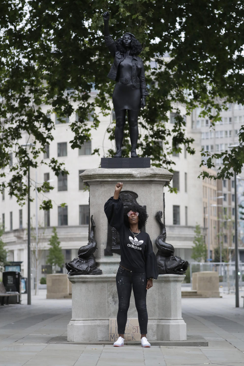 Jen Reid poses for photographs in front of the new black resin and steel statue portraying her, entitled "A Surge of Power (Jen Reid) 2020" by artist Marc Quinn after the statue was put up this morning on the empty plinth of the toppled statue of 17th century slave trader Edward Colston, which was pulled down during a Black Lives Matter protest in Bristol, England, Wednesday, July 15, 2020. On June 7 anti-racism demonstrators pulled the 18-foot (5.5 meter) bronze likeness of Colston down, dragged it to the nearby harbor and dumped it in the River Avon — sparking both delight and dismay in Britain and beyond. (AP Photo/Matt Dunham)