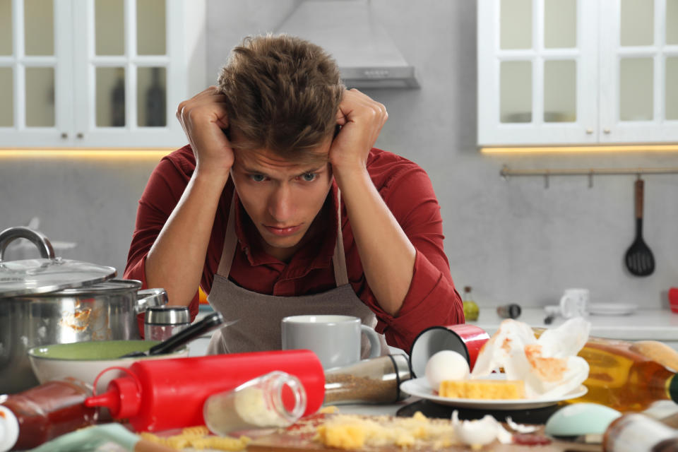 Man in kitchen looks stressed, surrounded by messy cooking ingredients and utensils