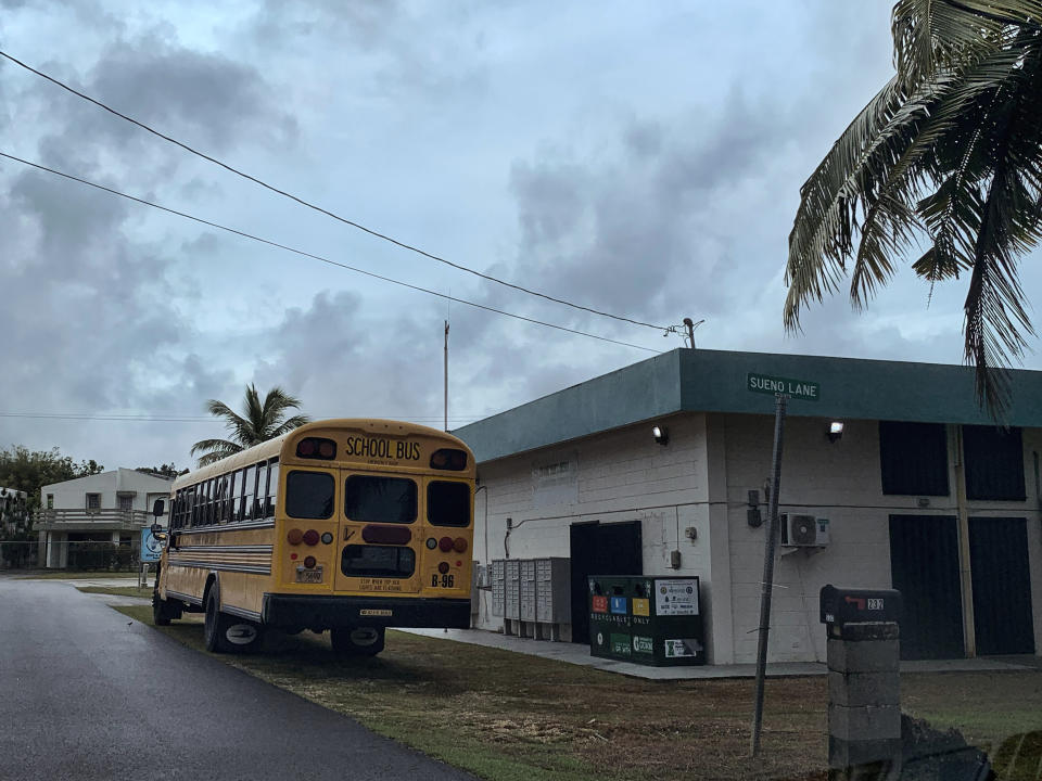 A school bus waits at the side of the Mongmong-Toto-Maite community center to transport residents to public schools set up as emergency shelters, Tuesday, May 23, 2023, in Guam, ahead of Typhoon Mawar. (AP Photo/Grace Garces Bordallo)
