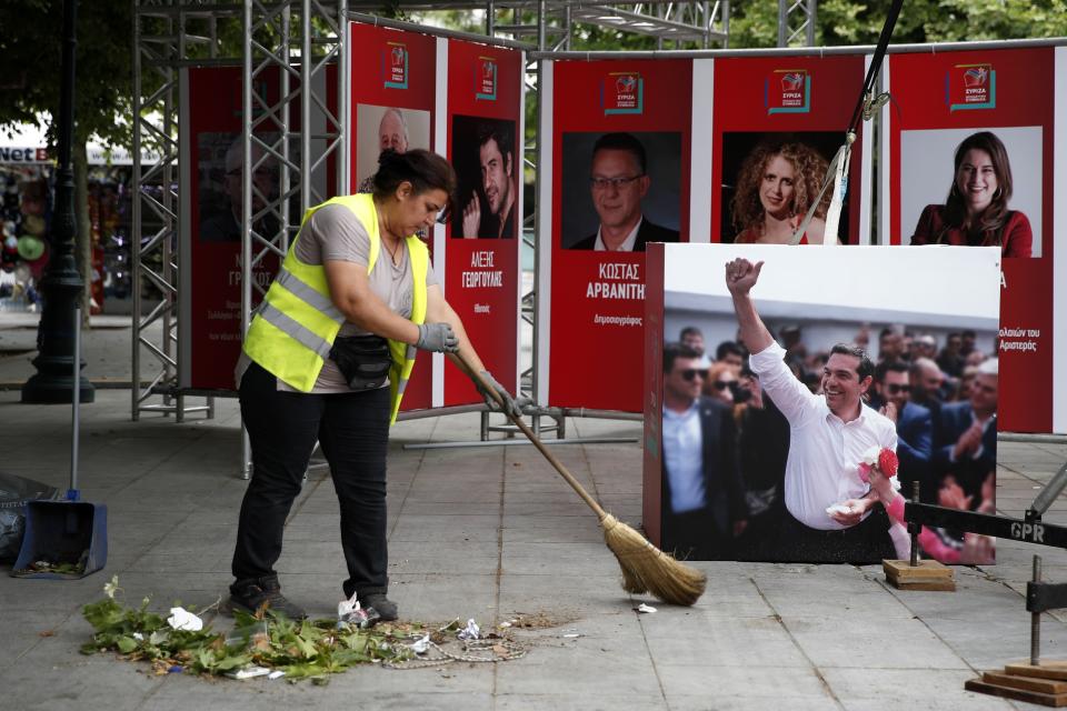 A photograph of Greece's Prime Minister Alexis Tsipras is displayed at a election kiosk of Syriza governing party as a municipal worker clears at Syntagma square in Athens, Monday, May 27, 2019. Tsipras called snap general elections following a resounding defeat of his left-wing Syriza party in European elections. (AP Photo/Thanassis Stavrakis)